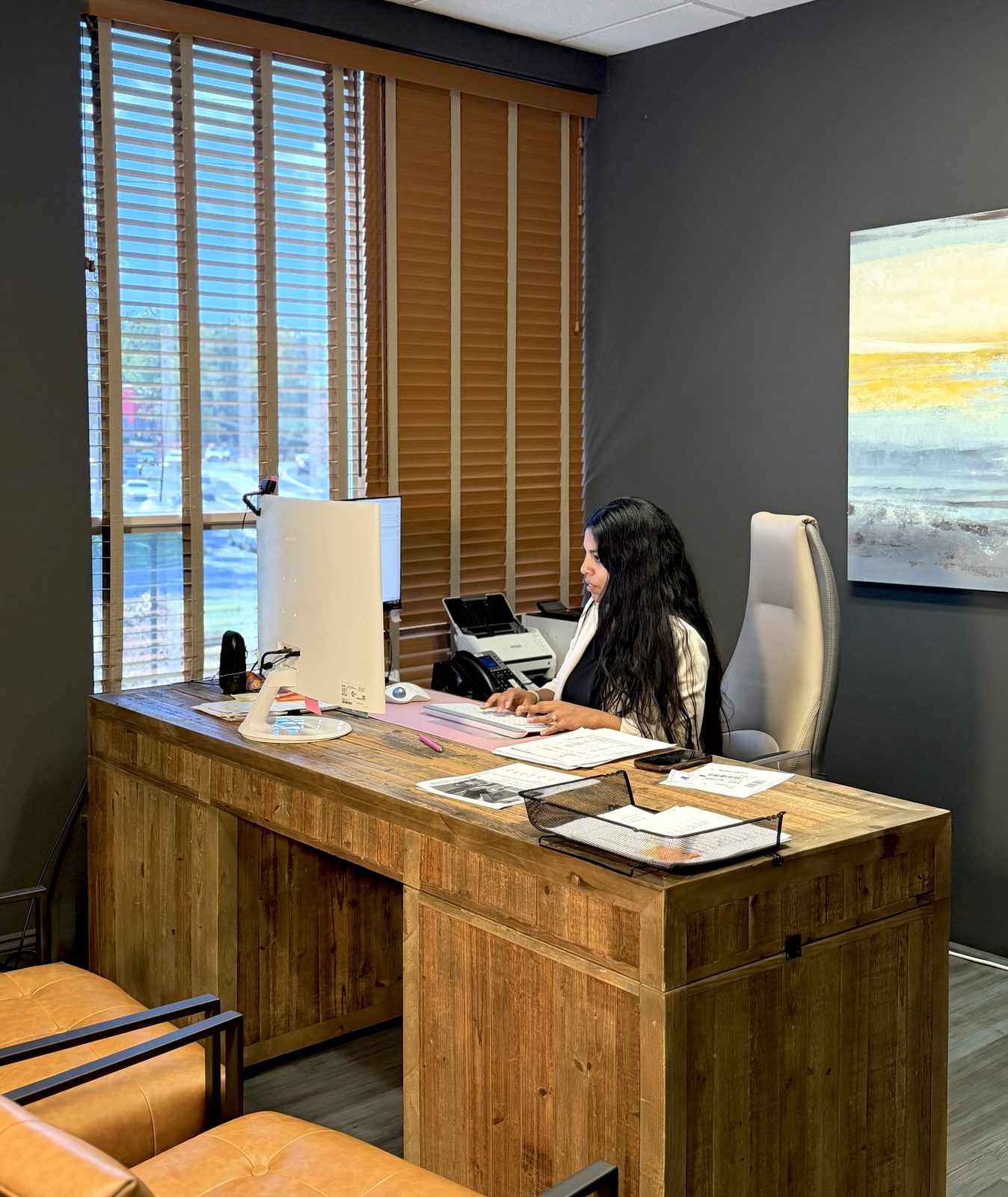 Una preparadora de Latorre & Company escribiendo en un escritorio de madera junto a una ventana, con un esc&aacute;ner y una bandeja de documentos de clientes